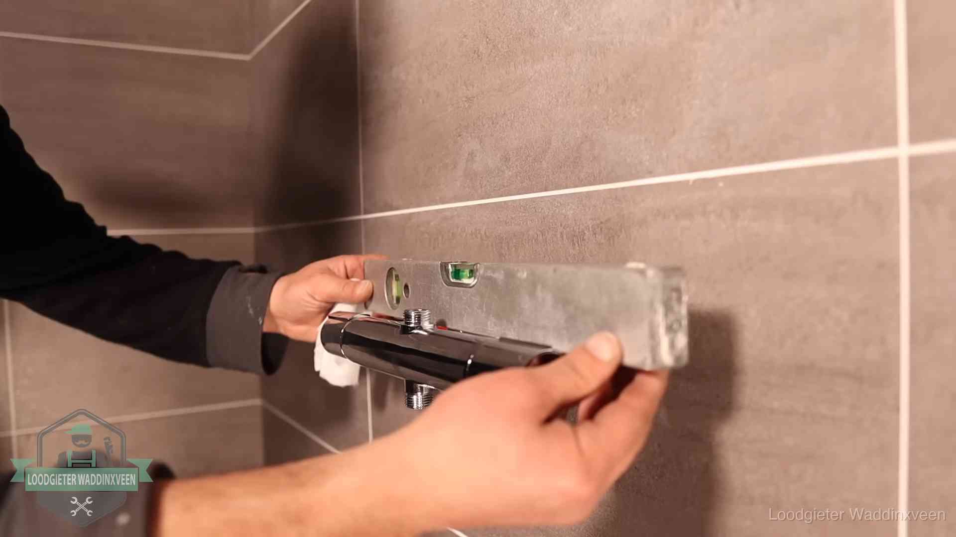 Loodgieter lijnt een douchekraan uit met een waterpas in een woning in Waddinxveen
