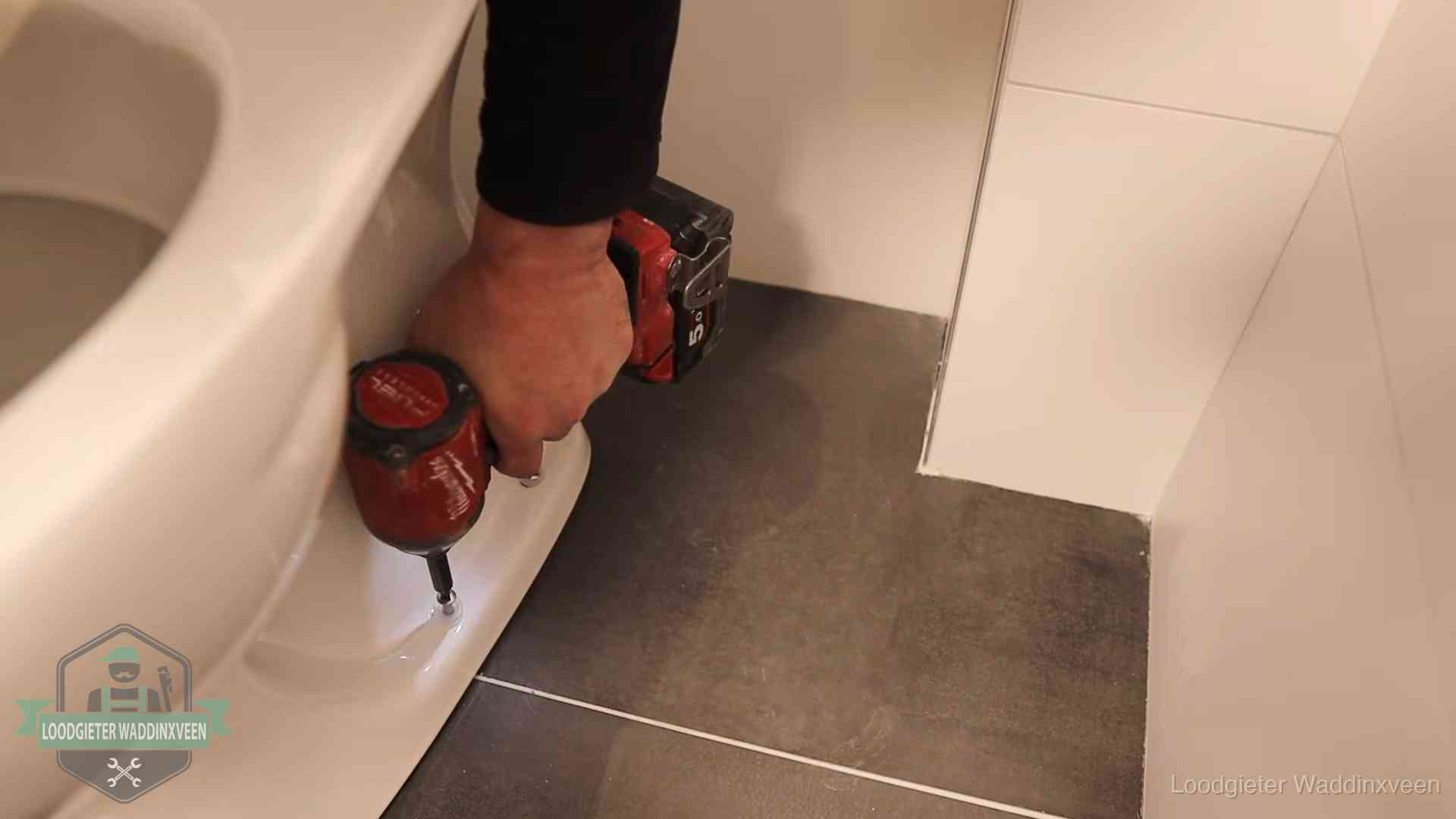 Kosten wc ontstoppen in Waddinxveen Loodgieter zet de voet van een wc-pot vast op de tegelvloer in Waddinxveen